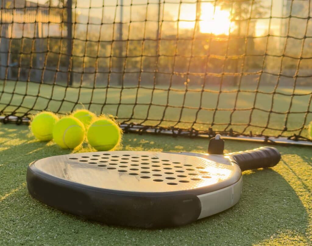 Raquette de padel avec balles de padel sur un terrain devant le filet