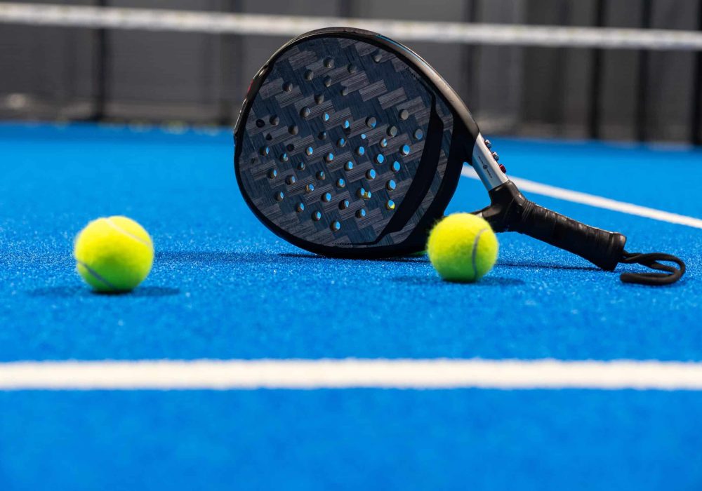 Black professional paddle tennis racket and ball with natural lighting on blue background. Horizontal sport theme poster, greeting cards, headers, website and app. High quality photo